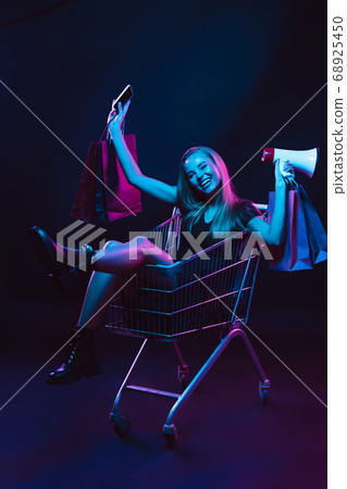Portrait of young woman in neon light on dark backgound. The human emotions, black friday, cyber monday, purchases, sales, finance concept. Portrait of young woman in neon light on dark backgound. The human emotions, black friday, cyber monday, purchases, sales, finance concept. 68925450
