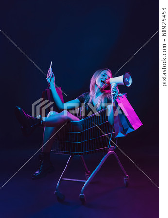 Portrait of young woman in neon light on dark backgound. The human emotions, black friday, cyber monday, purchases, sales, finance concept. Portrait of young woman in neon light on dark backgound. The human emotions, black friday, cyber monday, purchases, sales, finance concept. 68925453