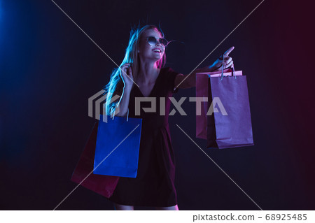 Portrait of young woman in neon light on dark backgound. The human emotions, black friday, cyber monday, purchases, sales, finance concept. Portrait of young woman in neon light on dark backgound. The human emotions, black friday, cyber monday, purchases, sales, finance concept. 68925485