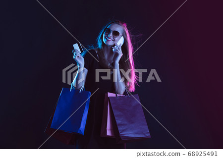 Portrait of young woman in neon light on dark backgound. The human emotions, black friday, cyber monday, purchases, sales, finance concept. Portrait of young woman in neon light on dark backgound. The human emotions, black friday, cyber monday, purchases, sales, finance concept. 68925491