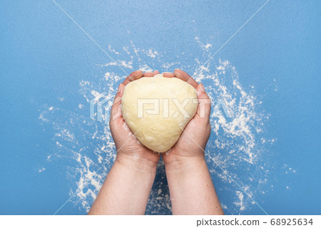 Raw dough held in hands over blue color. Uncooked Raw dough held in hands over blue color. Uncooked 68925634