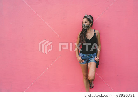 Asian woman leaning on pink wall wearing fabric face mask in fashion leopard pattern print. Casual young people city lifestyle during corona virus 68926351