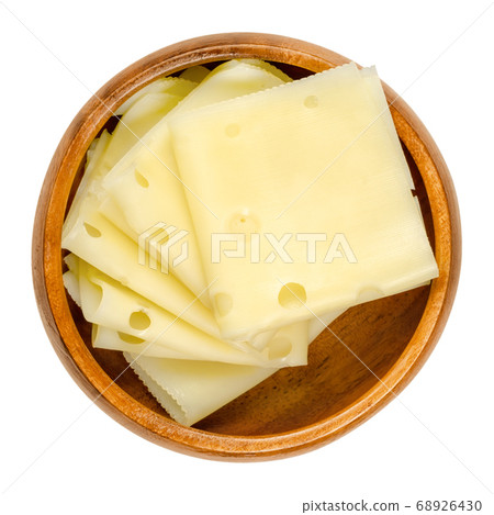 Emmental cheese slices in a wooden bowl. Folded slices of Emmenthal or Emmentaler. Yellow Swiss cheese with holes, medium-hard, with savory but mild taste. Close-up from above, over white, food photo. 68926430