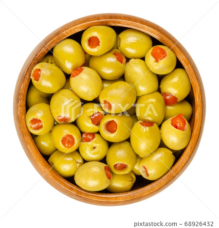 Pickled small green olives, filled with red sweet pepper in a wooden bowl. Fruits of Olea europaea, stuffed with bell pepper slices. Closeup from above, isolated on white background, macro food photo. Pickled small green olives, filled with red sweet pepper in a wooden bowl. Fruits of Olea europaea, stuffed with bell pepper slices. Closeup from above, isolated on white background, macro food photo. 68926432