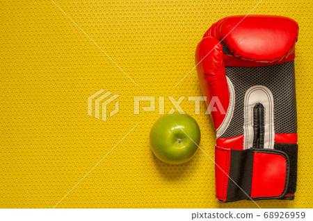 Top view of a green apple and red boxing glove on the yellow mat. Sport at home, fitness practice Top view of a green apple and red boxing glove on the yellow mat. Sport at home, fitness practice 68926959