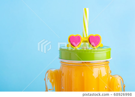 Cactus shape mason jar with orange juice. A jar with green lid and straw with sunglasses. 68926998