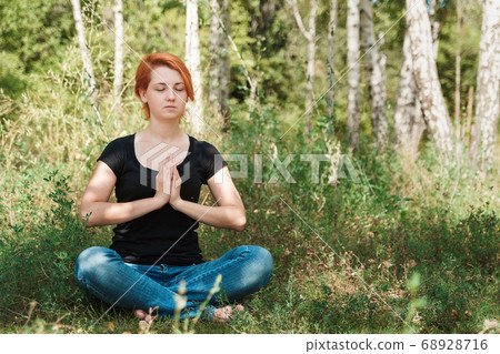 Cute ginger girl meditates in summer green forest. 68928716