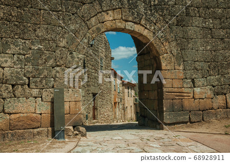 Old house seen through arch gate from a stone wall 68928911