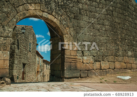 Old house seen through arch gate from a stone wall 68928913