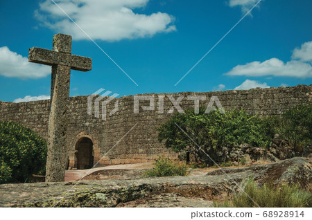 Cross made of stone over rocky terrain and large wall 68928914