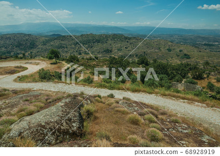 Road over hilly landscape covered by rocks 68928919