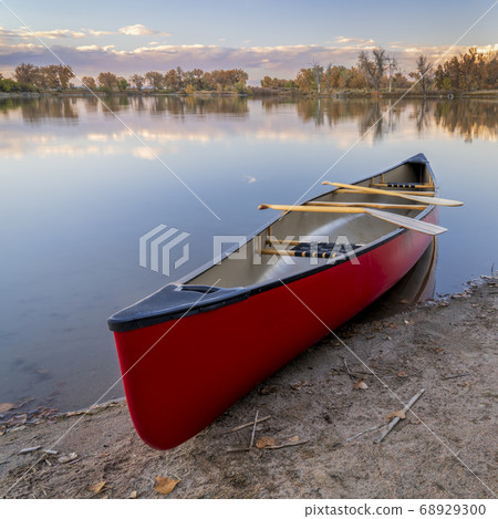 red canoe with paddles on a lake shore 68929300