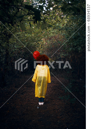 Woman in a yellow raincoat holding a red balloon on the background of forest. Woman in a yellow raincoat holding a red balloon on the background of forest. 68934537