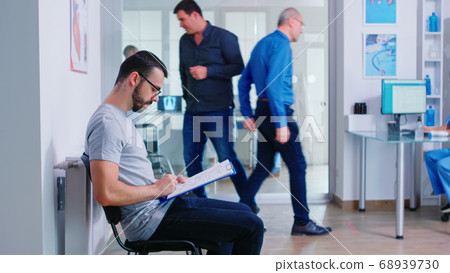 Young man filling documents in hospital waiting area Young man filling documents in hospital waiting area 68939730
