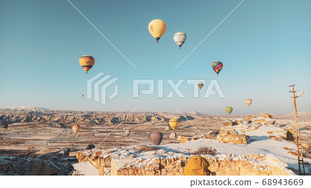 Colorful hot air balloons flying over the valley with fairy chimneys in winter season. Lots of Hot air balloons at the sunrise sky landscape in Cappadocia, Turkey 68943669