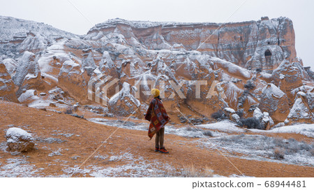 Woman alone with the volcanic landscape at Devrent Valley in Cappadocia. Girl walking around Fairy chimneys surronded by tufa formations at Imaginary Valley in winter season in Cappadocia, Turkey. Woman alone with the volcanic landscape at Devrent Valley in Cappadocia. Girl walking around Fairy chimneys surronded by tufa formations at Imaginary Valley in winter season in Cappadocia, Turkey. 68944481