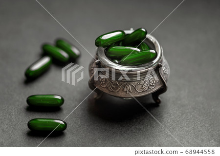 Green capsules with medicine in a silver bowl on a Green capsules with medicine in a silver bowl on a 68944558