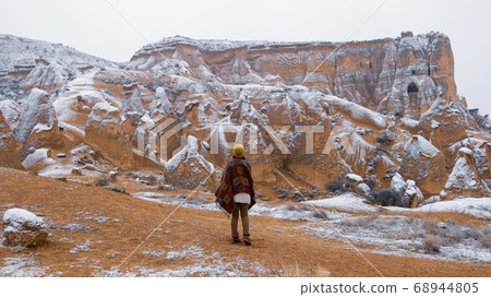 Woman alone with the volcanic landscape at Devrent Valley in Cappadocia. Girl walking around Fairy chimneys surronded by tufa formations at Imaginary Valley in winter season in Cappadocia, Turkey. 68944805