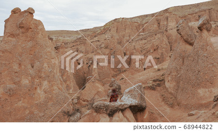 Woman alone with the volcanic landscape at Devrent Valley in Cappadocia. Girl walking around Fairy chimneys surronded by tufa formations at Imaginary Valley in winter season in Cappadocia, Turkey. Woman alone with the volcanic landscape at Devrent Valley in Cappadocia. Girl walking around Fairy chimneys surronded by tufa formations at Imaginary Valley in winter season in Cappadocia, Turkey. 68944822