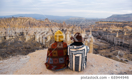 Travel couple watching mushroom shaped fairy chimneys at love valley in Cappadocia, Turkey. Happy couple watching the volcanic landscape at the valley of love in Goreme, Cappadocia Travel couple watching mushroom shaped fairy chimneys at love valley in Cappadocia, Turkey. Happy couple watching the volcanic landscape at the valley of love in Goreme, Cappadocia 68944946