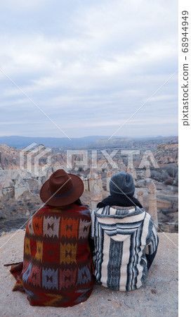 Travel couple watching mushroom shaped fairy chimneys at love valley in Cappadocia, Turkey. Happy couple watching the volcanic landscape at the valley of love in Goreme, Cappadocia 68944949