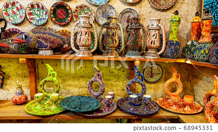 Hittite wine vessels, colorful ceramic vases and porcelain bowls in a underground cave atelier in Avanos in Cappadocia. Turkish traditional ceramic handycrafts in a local pottery shop in Cappadocia Hittite wine vessels, colorful ceramic vases and porcelain bowls in a underground cave atelier in Avanos in Cappadocia. Turkish traditional ceramic handycrafts in a local pottery shop in Cappadocia 68945331
