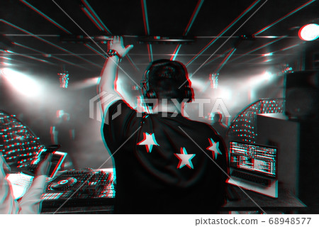 back of a male DJ with a raised hand in headphones 68948577
