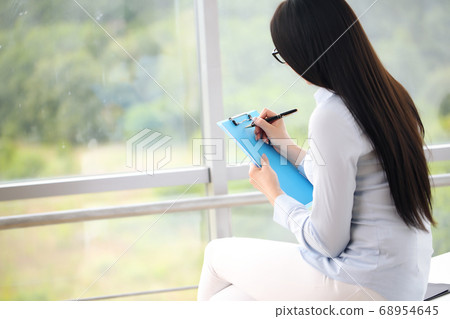 Smiling business woman sitting at desk with laptop and writing something in office Smiling business woman sitting at desk with laptop and writing something in office 68954645