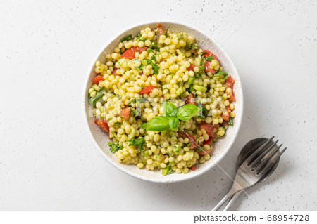 Pasta ptitim with vegetables decorated basil leaves on white. Top view. Space for text. Pasta ptitim with vegetables decorated basil leaves on white. Top view. Space for text. 68954728