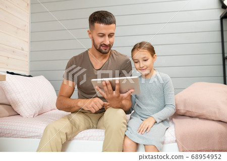Young smiling father with tablet sitting on bed next to his cute little daughter 68954952