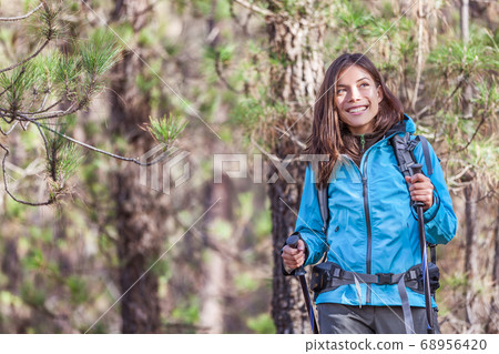 Happy hiker girl hiking in forest nature on hike trail in autumn outdoors travel vacations. Healthy lifestyle young Asian woman smiling portrait with poles, jacket, backpack Happy hiker girl hiking in forest nature on hike trail in autumn outdoors travel vacations. Healthy lifestyle young Asian woman smiling portrait with poles, jacket, backpack 68956420