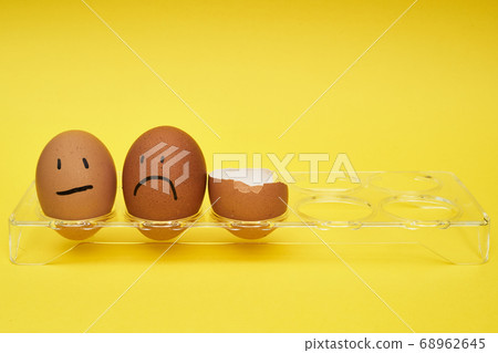 Chicken eggs in an egg holder. Full tray of eggs. Half an egg, egg yolk, shell. Emotion and facial expression painted on eggs. 68962645