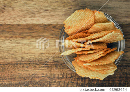 Corrugated potato chips on a wooden board. Snack, junk food. Close up. Corrugated potato chips on a wooden board. Snack, junk food. Close up. 68962654