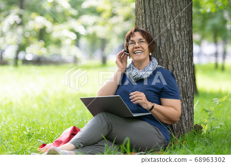 Happy middle-aged woman having online conversation on a laptop in the Park. 68963302