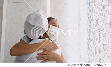 Smiling young female patient in mask with female doctor in white uniform thanking for help or feeling excited about healthcare treatment results at meeting. 68966149