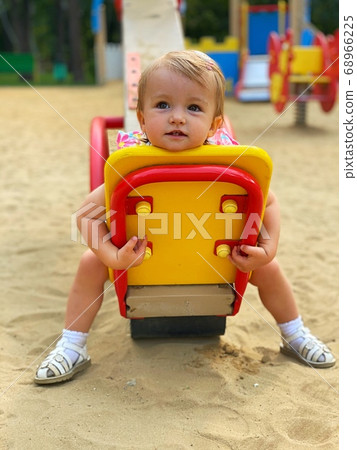 Cute little baby girl sits on a swing at the Cute little baby girl sits on a swing at the 68966225