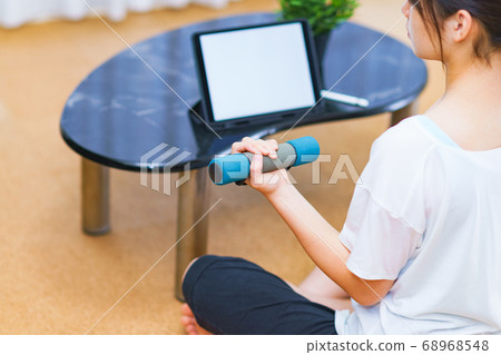 一名年輕女子，一邊觀看客廳裡播放的視頻一邊練啞鈴[新的正常生活方式] 68968548