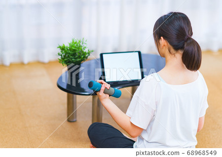 一名年輕女子，一邊觀看客廳裡播放的視頻一邊練啞鈴[新的正常生活方式] 68968549