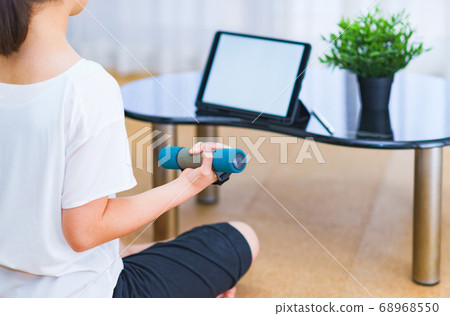 一名年輕女子，一邊觀看客廳裡播放的視頻一邊練啞鈴[新的正常生活方式] 68968550