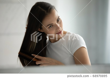 Close up head shot young woman combing hair with brush Close up head shot young woman combing hair with brush 68970895