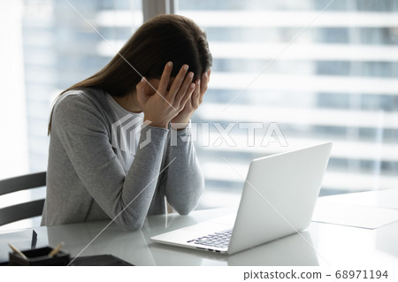 Frustrated overworked businesswoman covering face with hands, sitting at desk 68971194