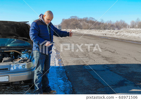 Upset young man hitchhiking and dialing for help 68971506