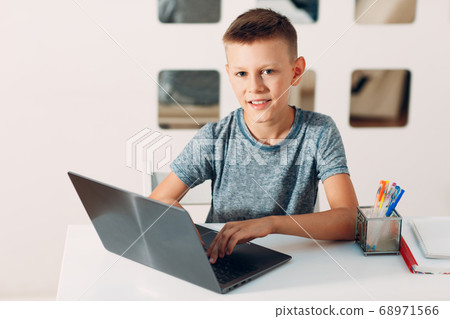 Young boy sitting at table with laptop and preparing to school at home. Online education concept. Young boy sitting at table with laptop and preparing to school at home. Online education concept. 68971566