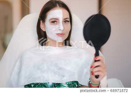 Beautiful woman with white mask on hulf of face. Attractive brunrtte woman in beauty salon Beautiful woman with white mask on hulf of face. Attractive brunrtte woman in beauty salon 68971872