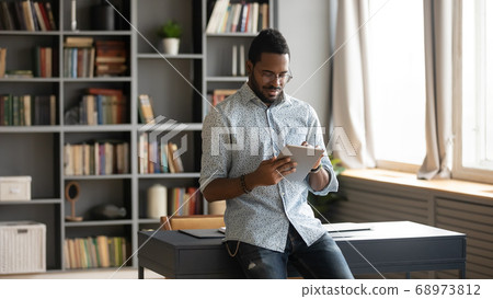 Focused African American man using computer tablet in modern cabinet 68973812