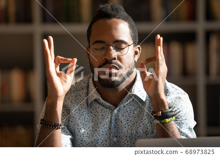 Close up mindful African American man wearing glasses meditating 68973825