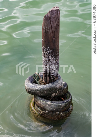 An old wooden pole in the sea with tires as An old wooden pole in the sea with tires as 68974390