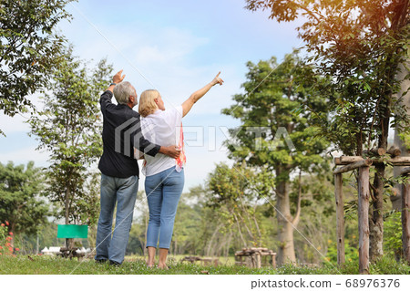 elderly couple pointing at something and embracing in park in summer time with sun light effect elderly couple pointing at something and embracing in park in summer time with sun light effect 68976376