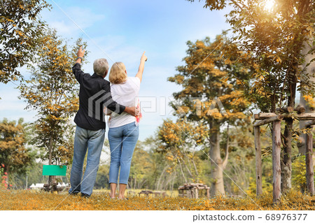elderly couple pointing at something and embracing in park in summer time with sun light effect elderly couple pointing at something and embracing in park in summer time with sun light effect 68976377
