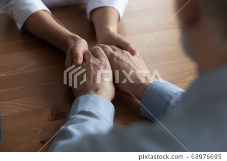 Close up young woman nurse holding hands of mature patient Close up young woman nurse holding hands of mature patient 68976695